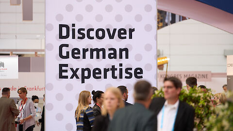 Messebesucher*innen und Infowand mit Schriftzug "Discover German Expertise" | © GCB / Patrick Kuschfeld
